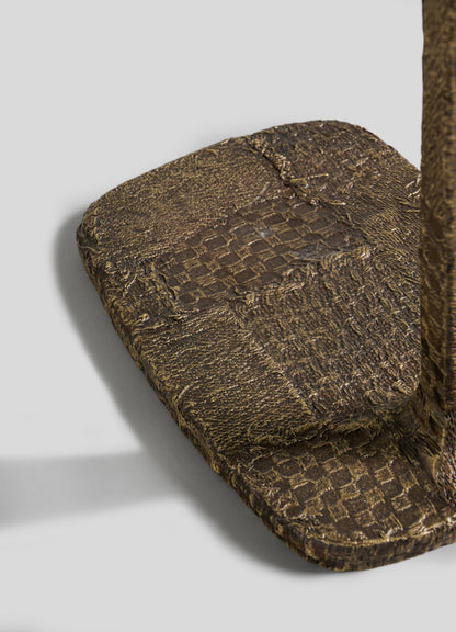 Close-up of the textured, cast brass base with a woven patchwork pattern on VIYA’s Mosaic Side Table B, supporting an upright structure against a plain light gray background.