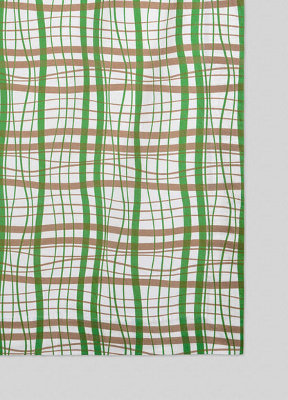 The Viya Madras Check Green & Beige Table Cloth features a wavy plaid of intersecting green and brown lines on white, blending contemporary tradition with classic Indian textiles for a striking optical illusion effect.