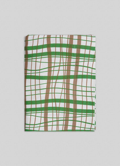 The Viya Madras Check Green & Beige Table Cloth features contemporary green, brown, and white checks, reflecting Indian textile tradition, and is shown folded on a light gray background.