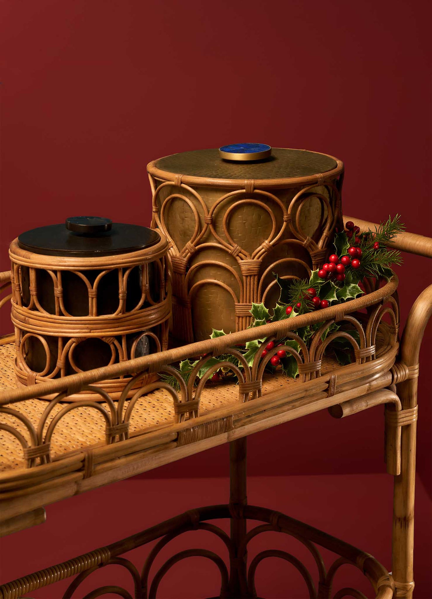The VIYA Nagaland Ice Bucket Small sits on a woven rattan cart against a burgundy backdrop, accented with a holiday sprig of holly and red berries.