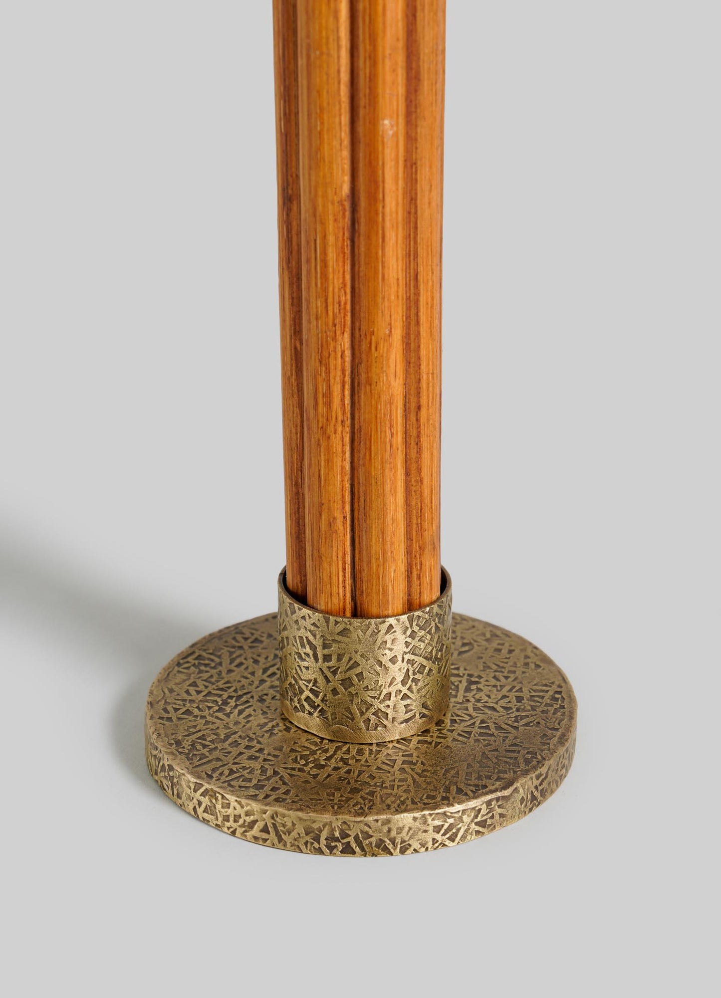 A close-up of the VIYA Namsai Candle Holder Small shows a wooden rod fitted into an ornate round metal base with detailed brass trim, set against a plain light gray background.