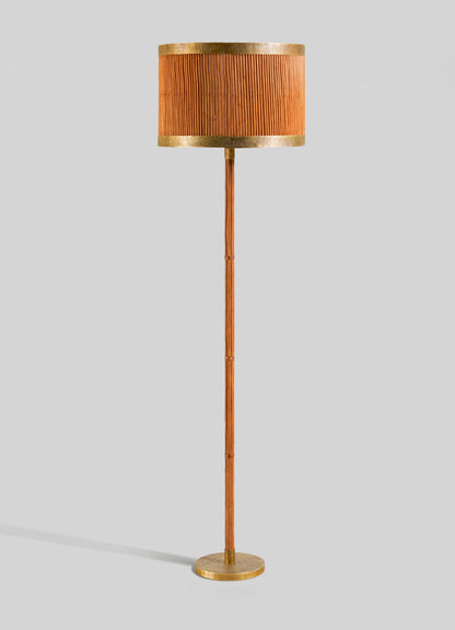 The VIYA Namsai Floor Lamp Round features a pleated orange lampshade, slender wooden pole, and circular gold base with brass accents, shown against a plain light grey background.
