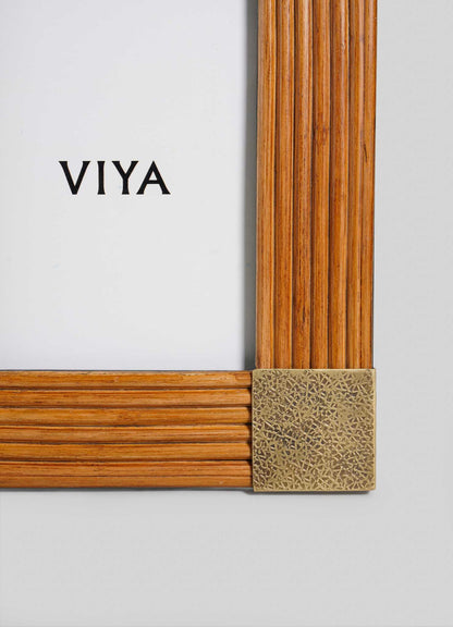 A close-up of the VIYA Namsai Photo Frame Large, a wooden frame with vertical and horizontal grooves, brass trimmings, and a decorative brass corner. The brand name VIYA is printed in black on a white background inside the frame.