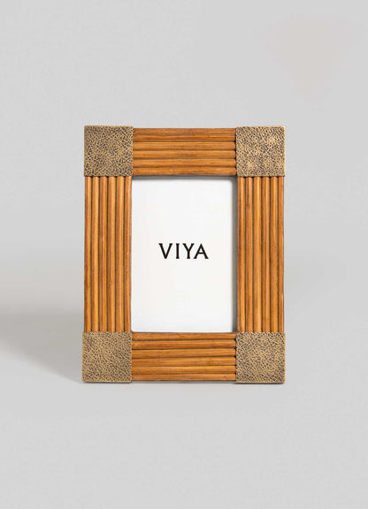 The Namsai Photo Frame Small by VIYA stands upright, featuring textured metallic corners and brass trimmings. It displays a white paper with "VIYA" in bold black letters against a plain gray background.