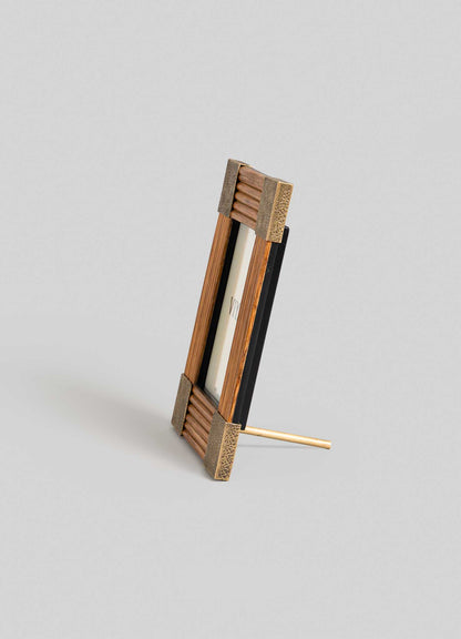 The VIYA Namsai Photo Frame Small features brass trimmings and metal corner accents, standing upright at an angle on a light gray surface with support from a back stand.