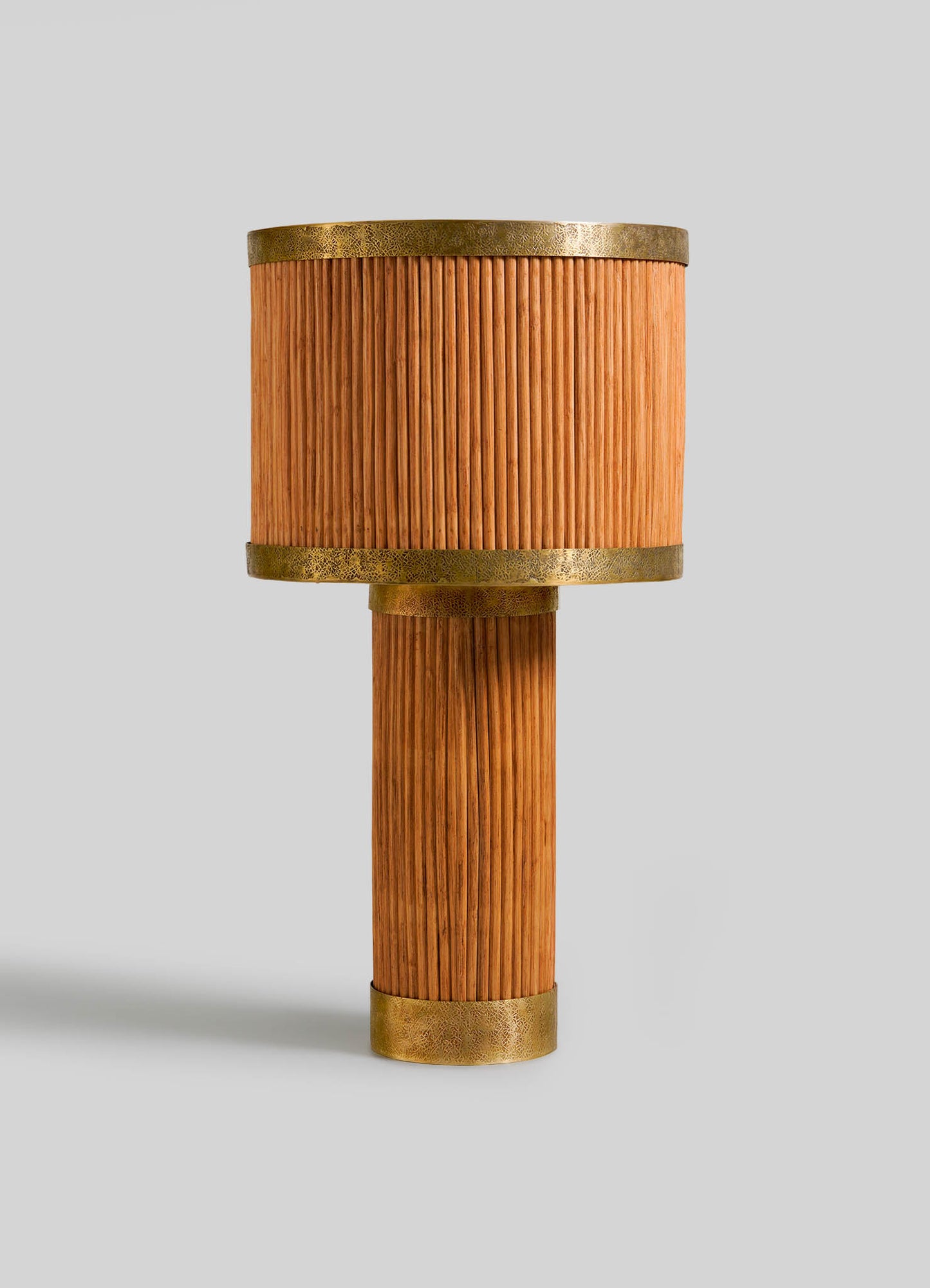 The VIYA Namsai Table Lamp Round features a cylindrical base and shade with vertical wood slats inspired by cane weaving, accented with metallic gold bands, and is shown against a plain light gray background.