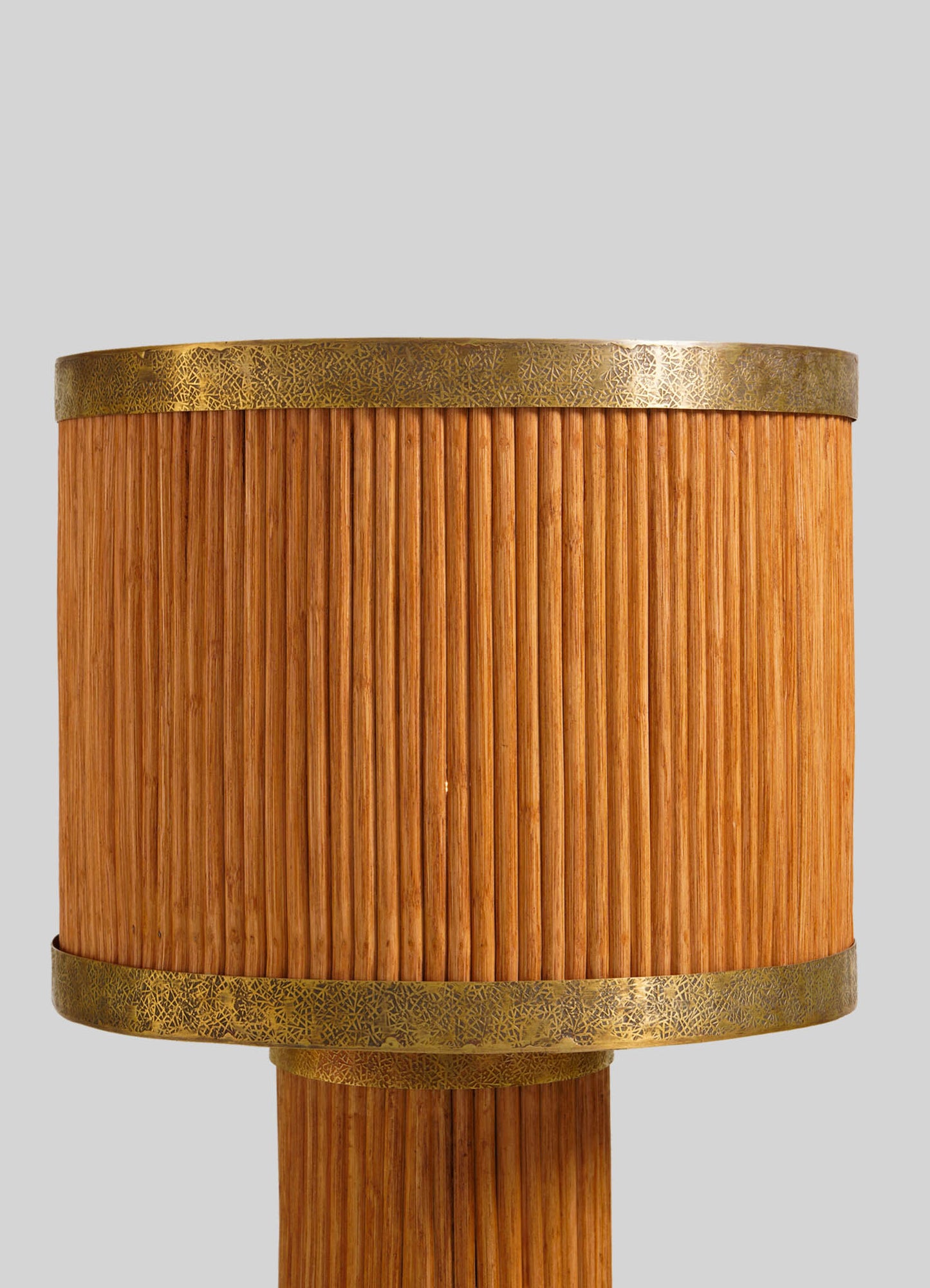 A close-up of the VIYA Namsai Table Lamp Round features vertical wooden slats bordered with brass bands bearing delicate patterns, reflecting traditional cane weaving artistry, set against a plain light gray background.