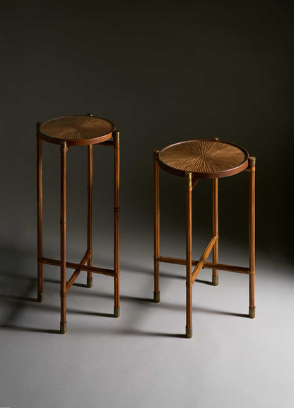 Two tall Namsai Tray Tables by VIYA feature sunburst-patterned wooden tops and slender, bamboo-like legs with subtle brass accents, standing on a gray surface against a dark background.
