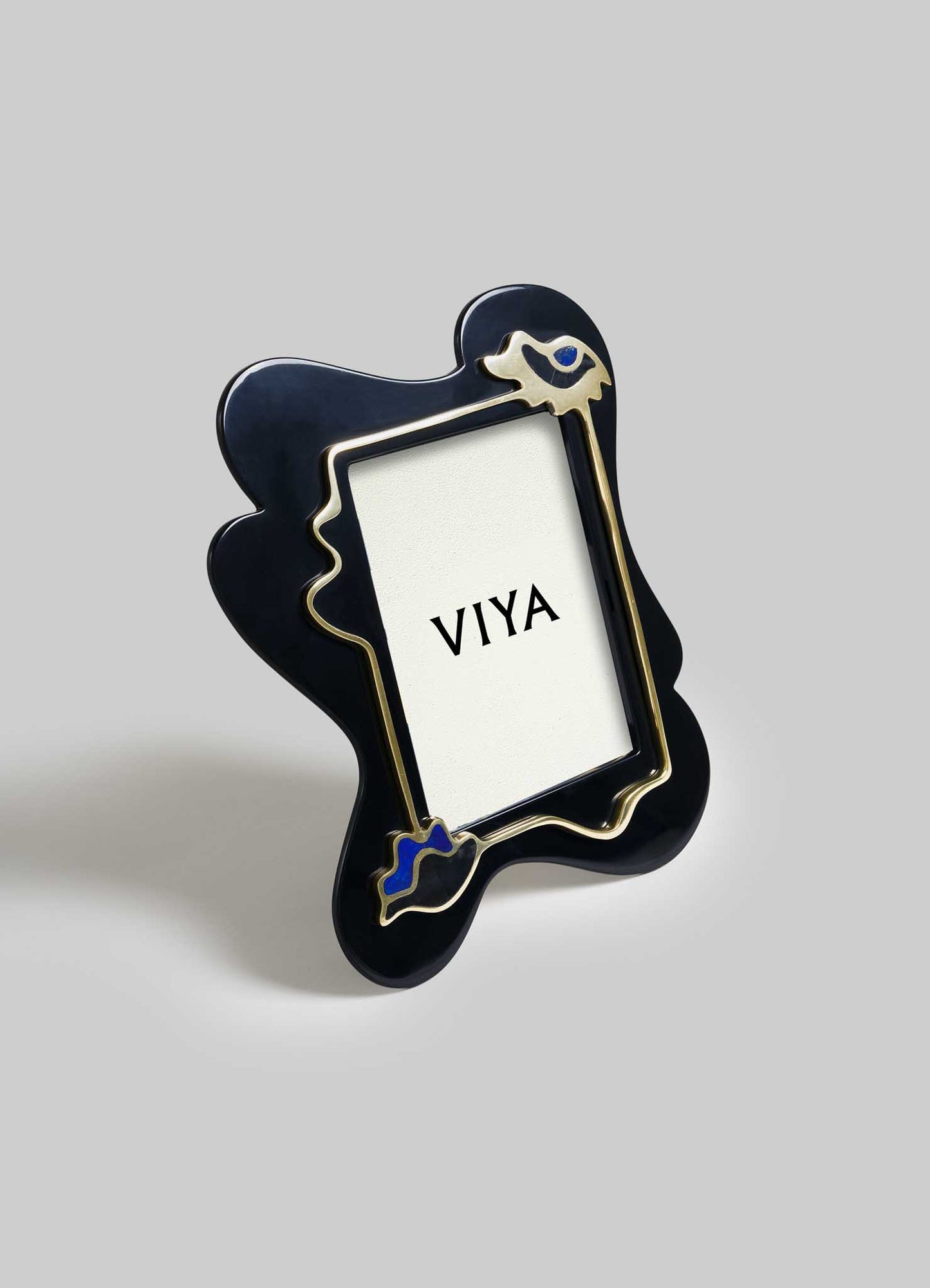 The VIYA Nazar Black Photo Frame features abstract curvy edges, a gold outline, and blue accents inspired by a Nazar amulet, and is pictured standing on a gray surface.