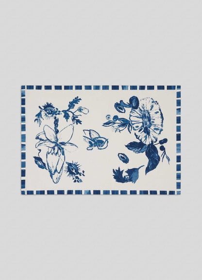 The Viya Orchard Blue Placemats - Set of 4 feature a rectangular white design with hand-painted blue floral patterns and a striped border, inspired by Indian fruit orchard motifs like wood apple and pomegranate.
