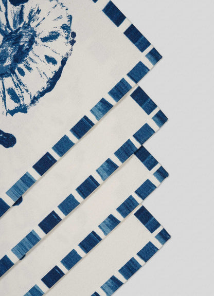 Four Orchard Blue Placemats by Viya are stacked diagonally. The cream-colored set features blue checkered borders and an abstract floral motif, inspired by Indian orchards, against a light background. Set includes 4 placemats.