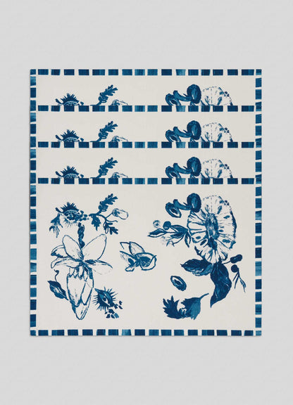 The Viya Orchard Blue Placemats - Set of 4 feature rectangular white mats with blue botanical and floral patterns inspired by an Indian fruit orchard, showcasing various flowers, leaves, and a checked blue border.