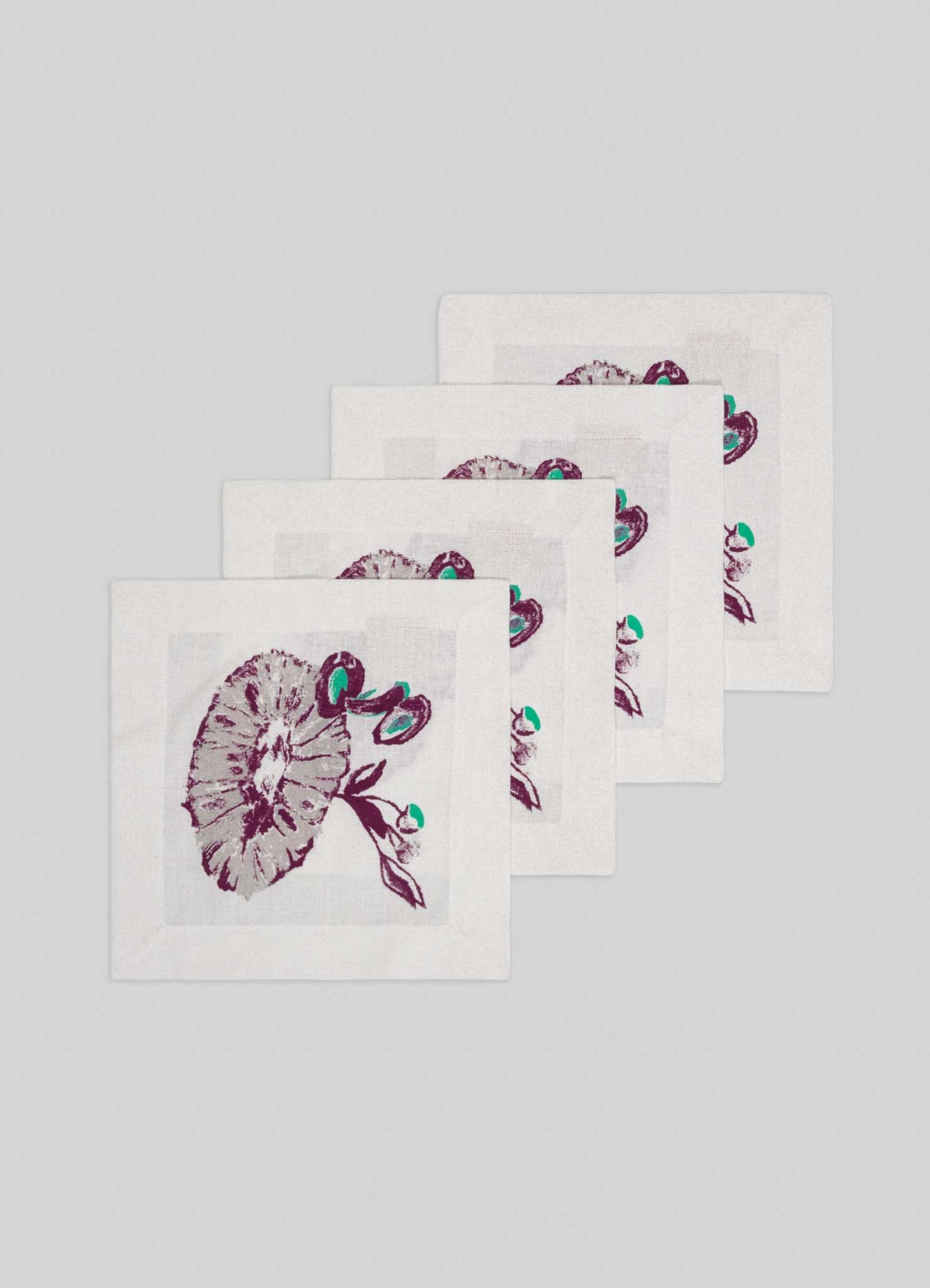 The Viya Orchard Green Cocktail Napkins – Set of 4 – feature printed purple and teal mushroom and leaf designs on white cloth, arranged in an overlapping row against a light gray background.