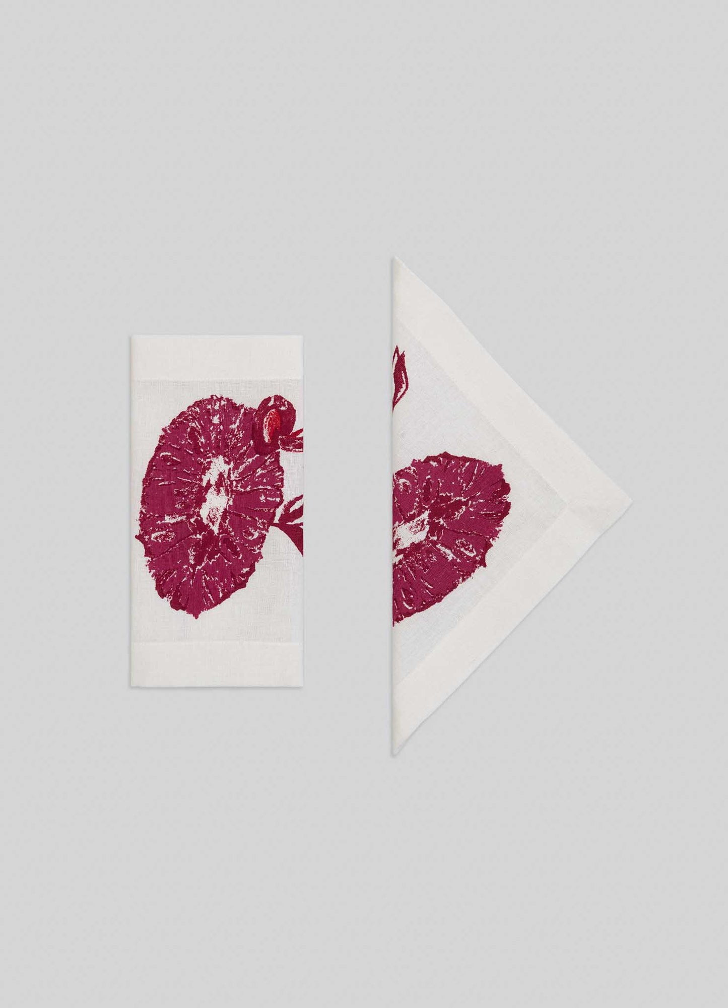 The Viya Orchard Red Cocktail Napkins – Set of 4, featuring red Indian pomegranate-inspired floral prints on white fabric, are displayed folded in half and as a triangle against a light gray background.