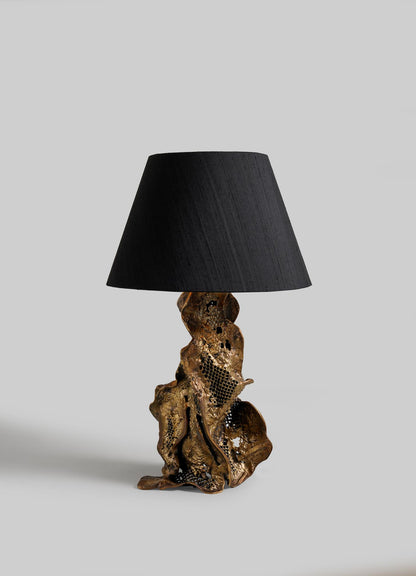 The VIYA Palash Table Lamp features a sculptural, twisted metallic base inspired by driftwood and a wide black shade, shown against a plain light grey background.