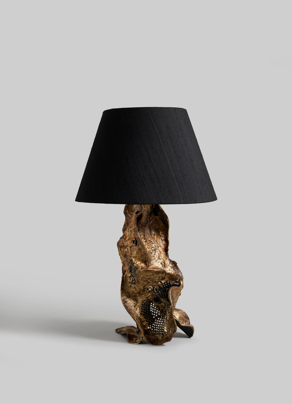 The VIYA Palash Table Lamp features a textured gold sculpted base with an abstract design and a simple black lampshade, shown against a plain gray background.
