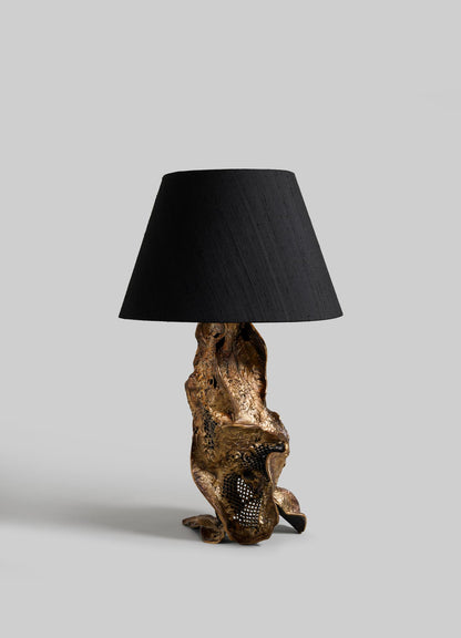 The VIYA Palash Table Lamp features a textured gold sculpted base with an abstract design and a simple black lampshade, shown against a plain gray background.