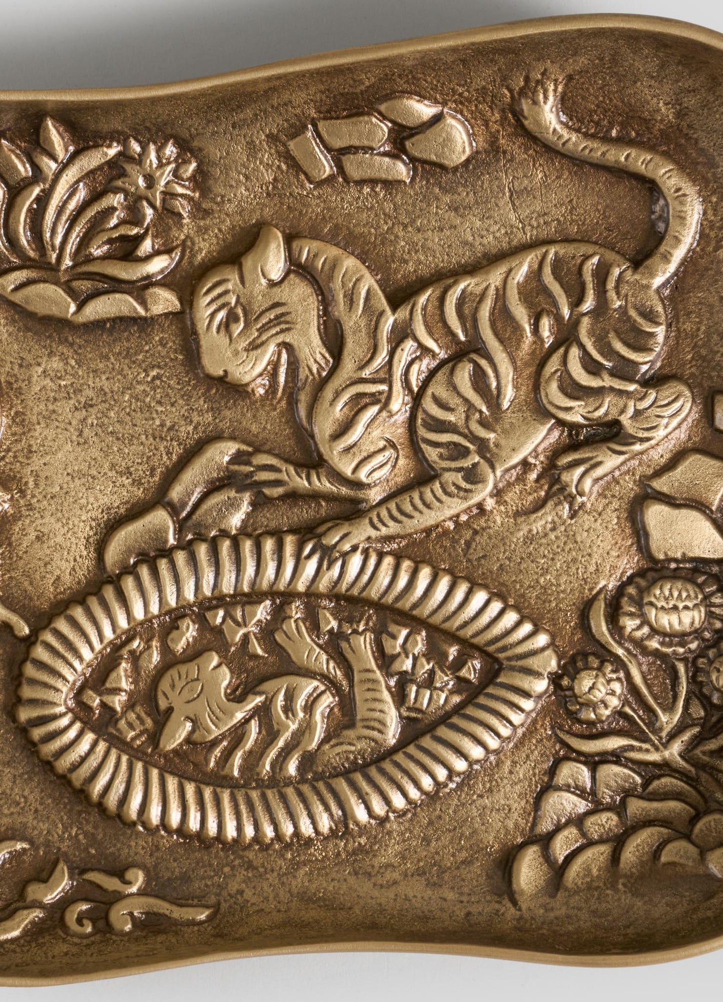 A close-up of the VIYA Tiger & Hare Trinket Tray shows a decorative brass design with a raised tiger, plants, and ornate patterns—intricate details that make it a unique jungle-inspired catch-all accent.