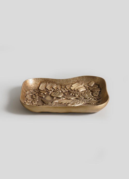 The VIYA Panchatantra Tortoise Trinket Bowl is a rectangular brass dish with raised, intricate detailing and a tortoise design on the inner surface, displayed against a plain light gray background.