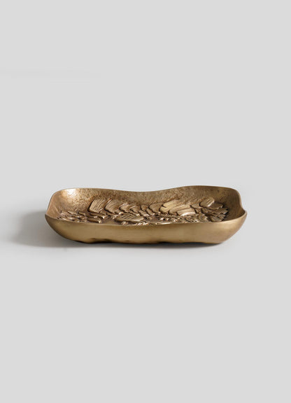 The VIYA Tortoise & Crane Trinket Bowl is a rectangular, shallow brass tray with wavy edges and a raised leaf pattern, shown against a plain light gray background.