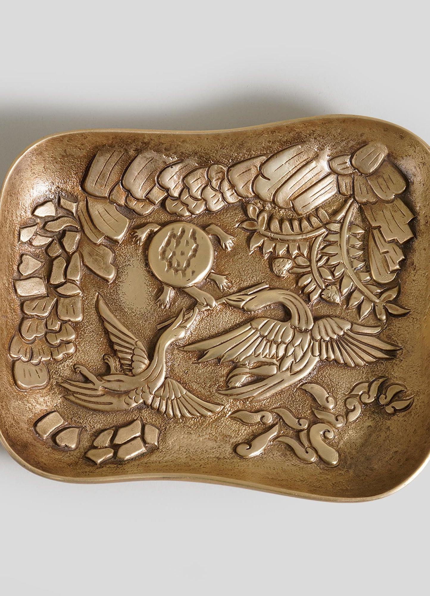 The VIYA Tortoise & Crane Trinket Bowl is a square, gold-toned metal tray with a raised crane, sun, and clouds design—ideal as a brass catch-all or unique decor accent inspired by jungle fables.