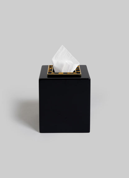 The VIYA Plaza Cube Tissue Box features a black, square design with a gold-trimmed opening, inspired by Art Deco elegance. A single white tissue peeks from the top against a plain gray background.