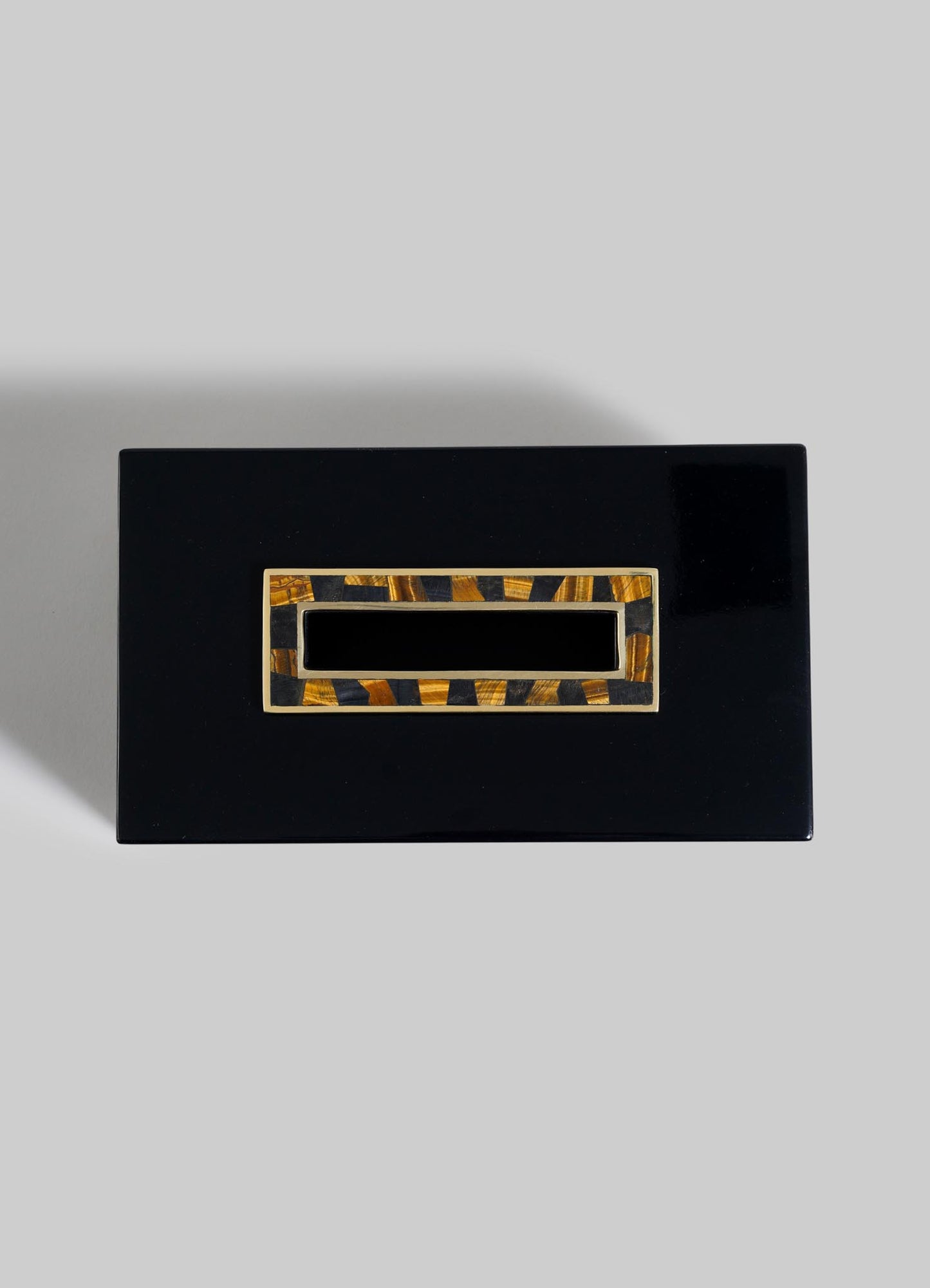 A rectangular, glossy black VIYA Plaza Tissue Box with an Art Deco-inspired gold and brown clasp, evoking Bombay's vintage cinema halls, is displayed against a plain grey background.