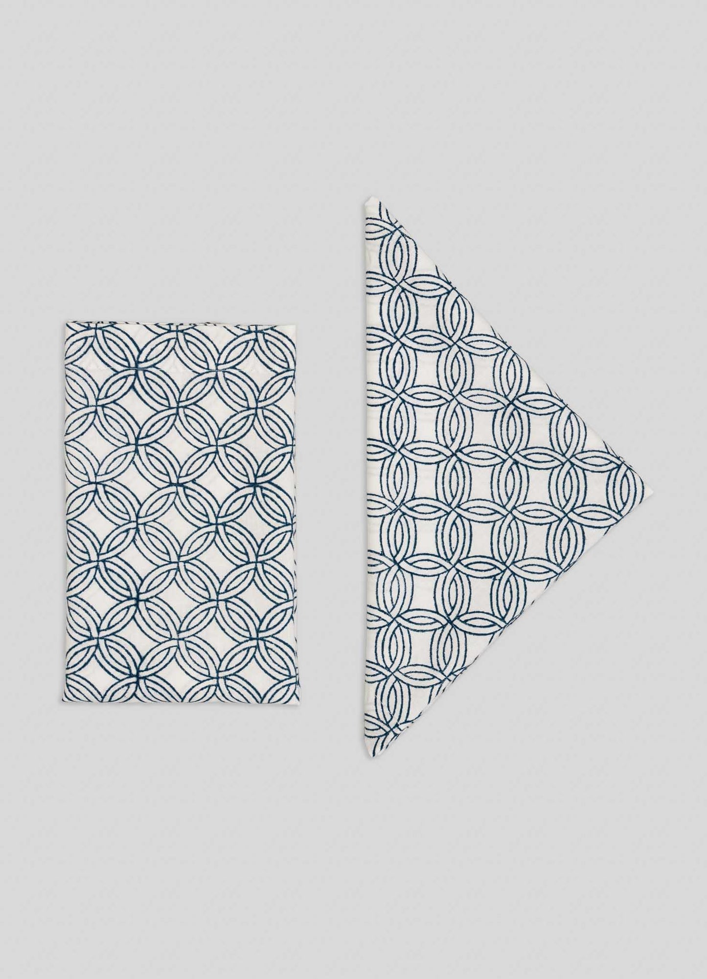 Set of 4 Paigah Navy Napkins by Viya, featuring white cloth with navy blue overlapping circular patterns inspired by Indo-Islamic Hyderabadi architecture. Shown folded in both rectangle and triangle shapes on a light background.