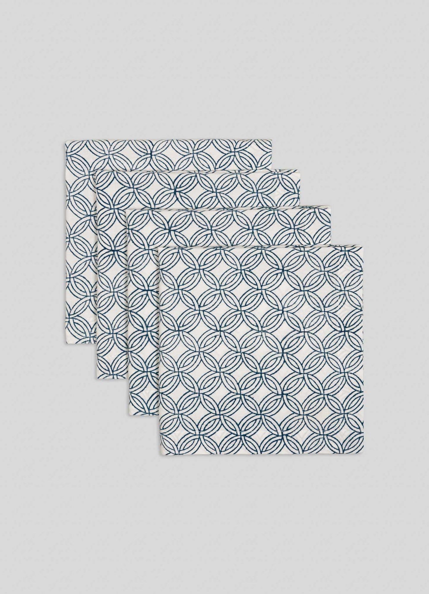 The Viya Paigah Navy Napkins - Set of 4, featuring a blue overlapping circle motif inspired by Hyderabad’s paigah jaalis, are neatly stacked in a fanned arrangement on a light grey background.