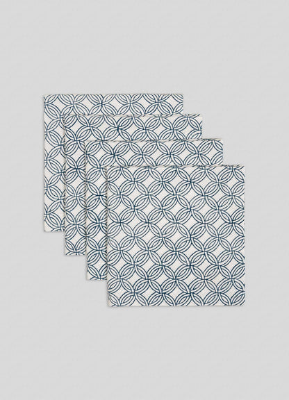 The Viya Paigah Navy Napkins - Set of 4, featuring a blue overlapping circle motif inspired by Hyderabad’s paigah jaalis, are neatly stacked in a fanned arrangement on a light grey background.