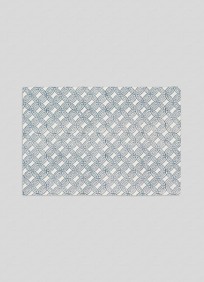 The Viya Paigah Navy Placemats – Set of 4 features a rectangular white design with overlapping blue circles, inspired by Hyderabad's Paigah jaalis, set against a plain light gray background.