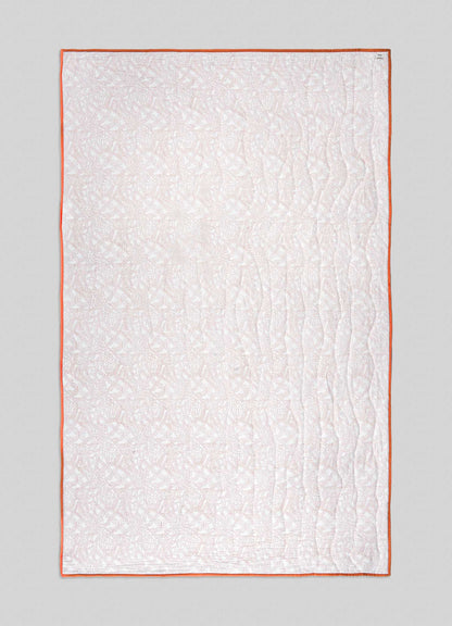 The Viya Paigah Orange & Blue Single Quilt is rectangular and light-colored, with an intricate lattice pattern, orange edging, and gentle wavy vertical stitches, displayed on a plain gray background.