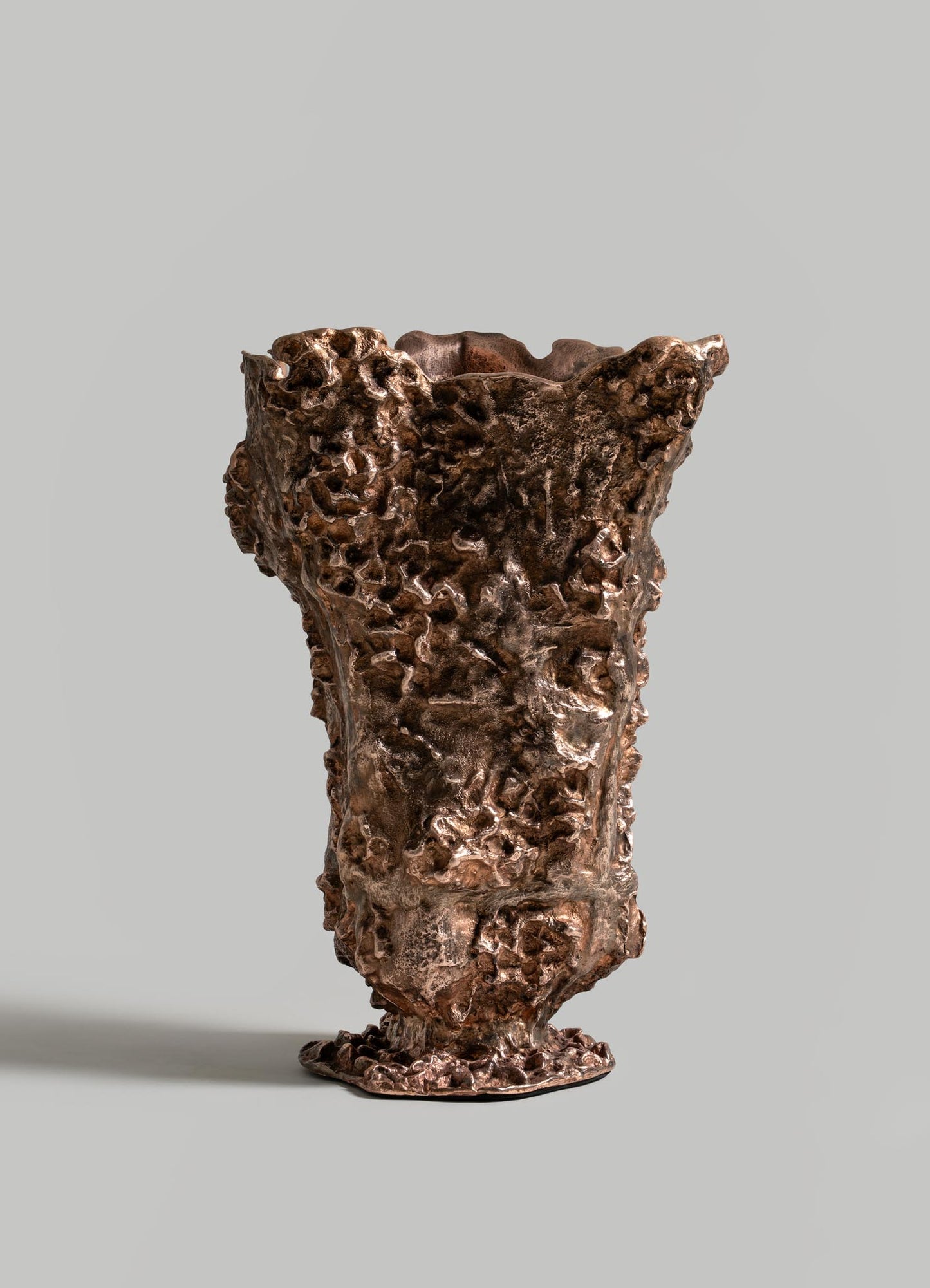 The VIYA Red Earth Vase, featuring a sculptural bronze design with an uneven, coral-like texture, stands upright against a plain gray background—an ideal accent for a sculptural table or forest-inspired furniture.