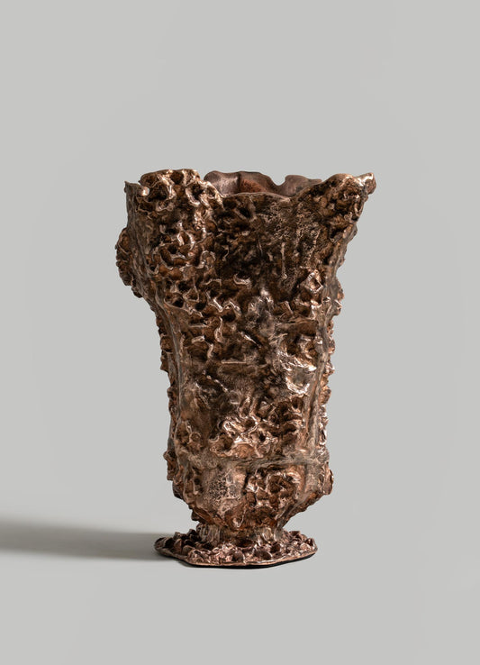 The VIYA Red Earth Vase, featuring a sculptural bronze design with an uneven, coral-like texture, stands upright against a plain gray background—an ideal accent for a sculptural table or forest-inspired furniture.