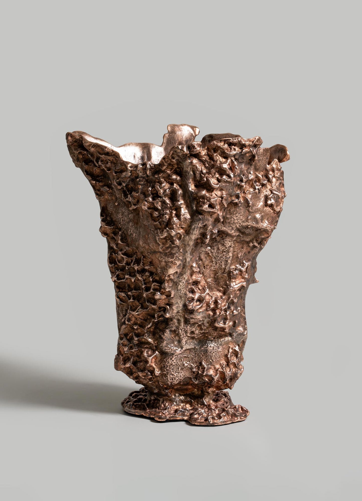 The VIYA Red Earth Vase, with a bronze hue, textured organic surface, and irregular edges, rests on a sculptural table against a plain light gray background.