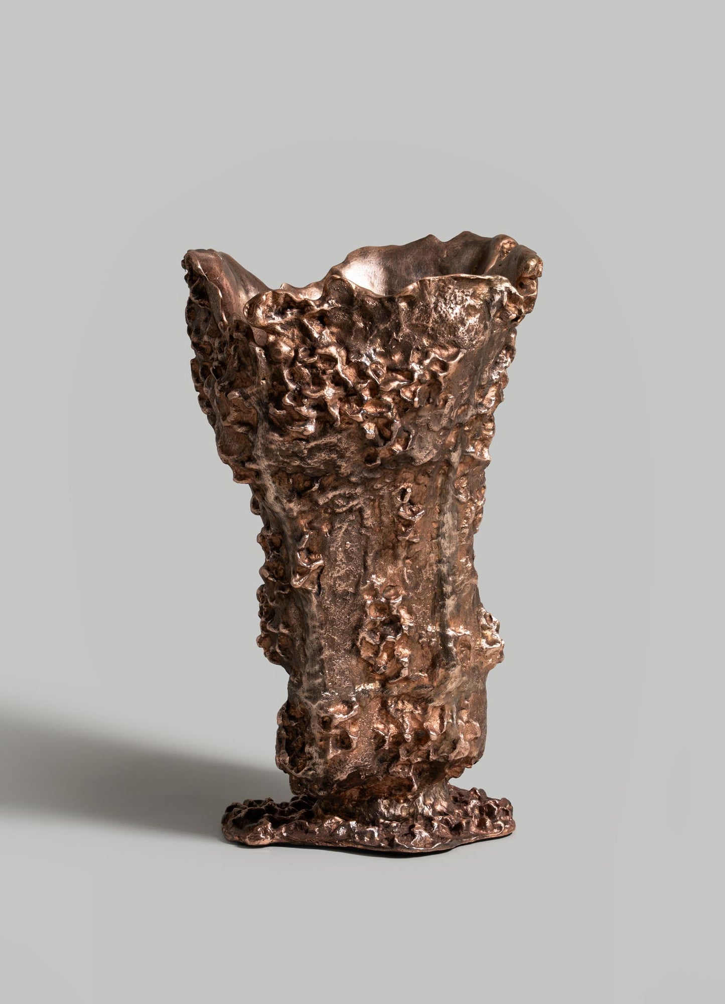 The VIYA Red Earth Vase features a bronze, textured surface with irregular edges and a rugged, organic form. It stands upright on a smooth gray background, reflecting forest-inspired artistry.