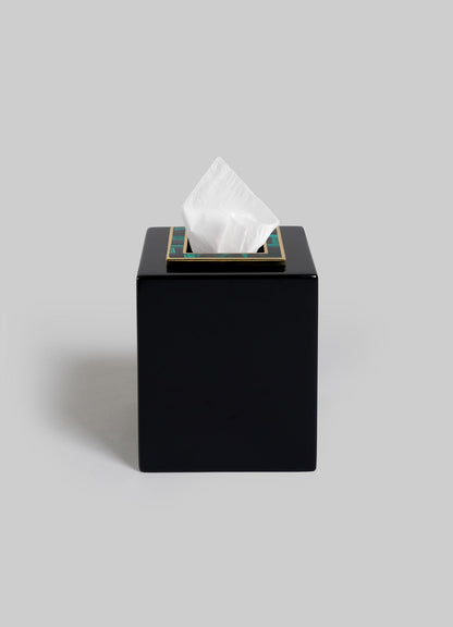 The VIYA Rivoli Cube Tissue Box, featuring a black square design with a gold-trimmed opening, evokes Art Deco elegance as a single white tissue emerges from the top against a plain gray background.