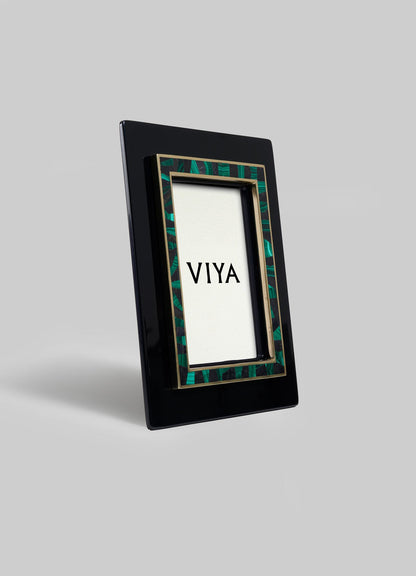 The Rivoli Photo Frame by VIYA features a glossy black rectangular border with a green and gold Art Deco-inspired inner trim. Displayed upright, it evokes vintage Bombay cinema halls against a plain light gray background.