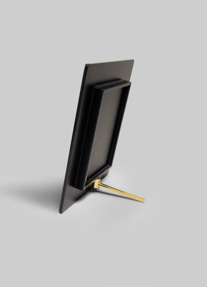 The VIYA Rivoli Photo Frame, inspired by Art Deco details from old Bombay cinema halls, is shown in black with a gold stand on a light gray background. The empty frame is vertically oriented and displayed from the back.