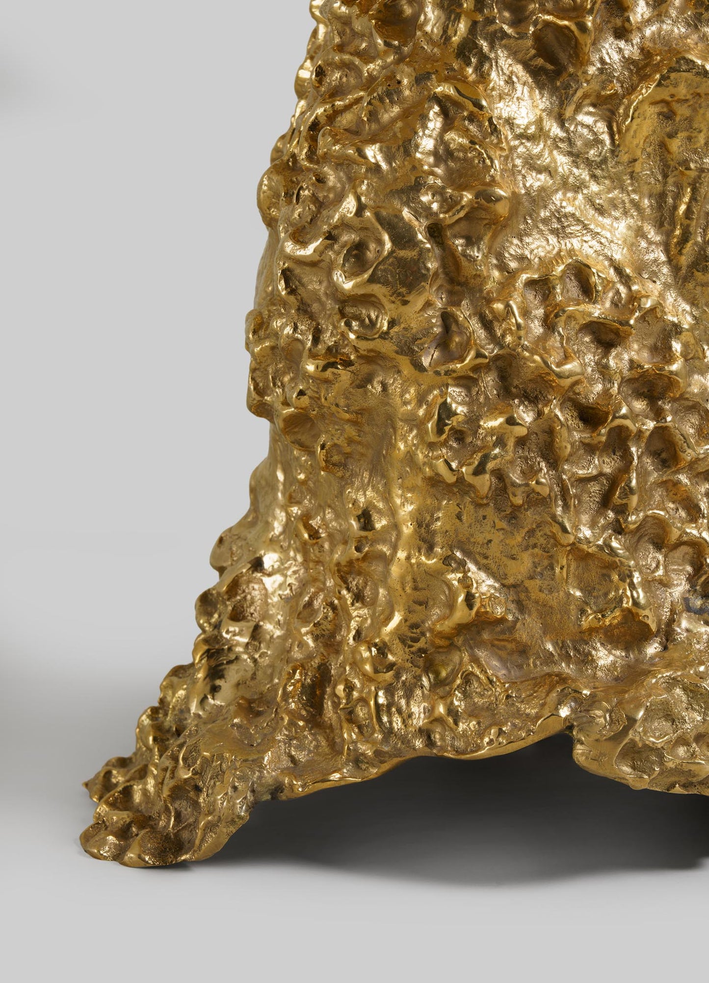 Close-up of VIYA’s Red Earth Table Lamp in gold, featuring a textured, sculptural surface that recalls molten metal or organic forms. Set against a plain light gray background.