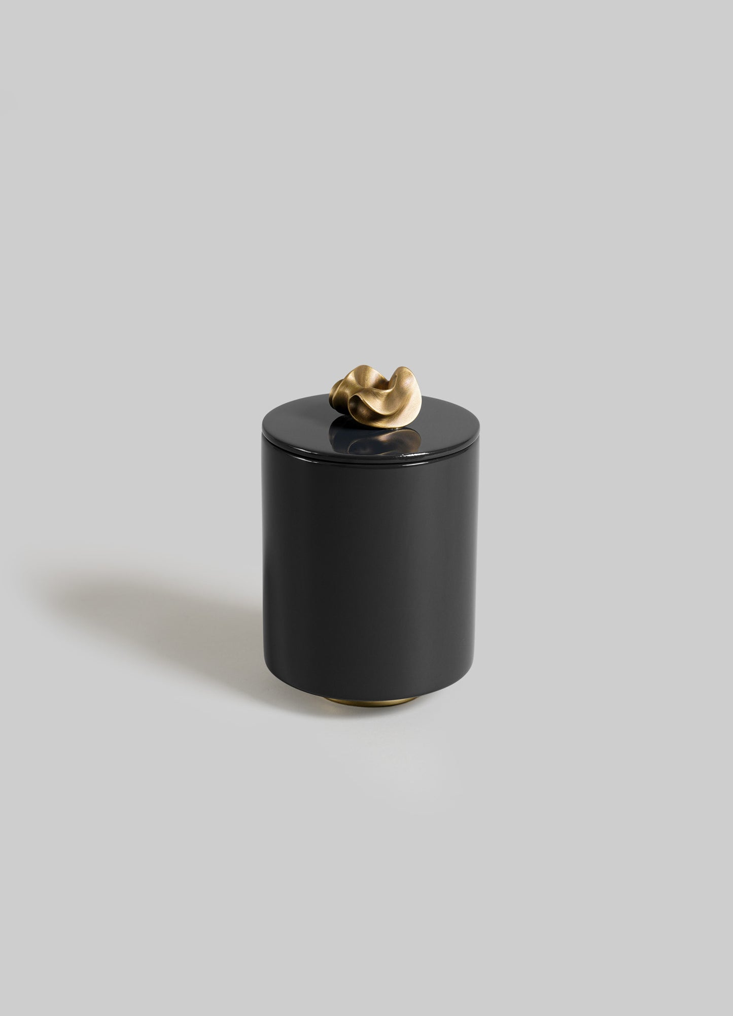 The VIYA Saffron Black Round Container features a sleek black cylindrical design with a smooth finish and a sculptural gold knob lid, inspired by saffron threads, shown against a plain light gray background.