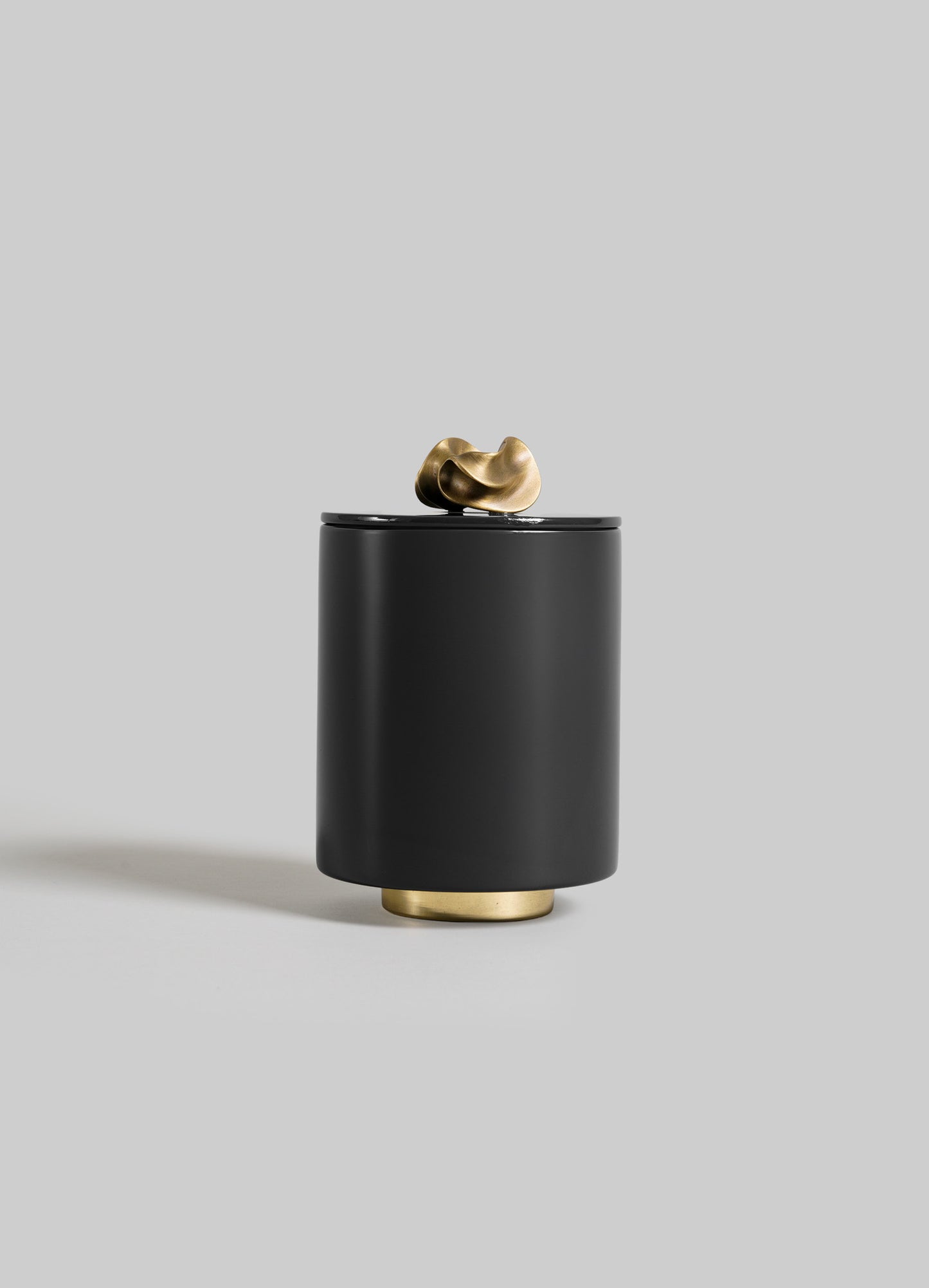 The VIYA Saffron Black Round Container is a sleek, matte black cylindrical container with a small gold base and textured gold handle on the lid, perfect for storing saffron threads, shown against a plain light gray background.