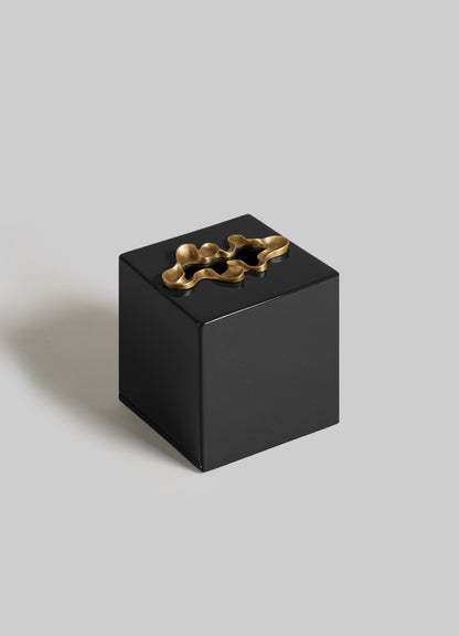 The VIYA Saffron Black Tissue Box Small features a glossy black finish and a sculptural gold metallic lid accent, echoing contemporary bronzed art, shown against a plain light gray background.