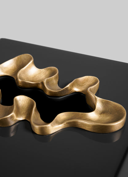 Close-up of the VIYA Saffron Black Tissue Box Small, a contemporary, gold-accented accessory resting on a glossy black surface against a plain grey background.