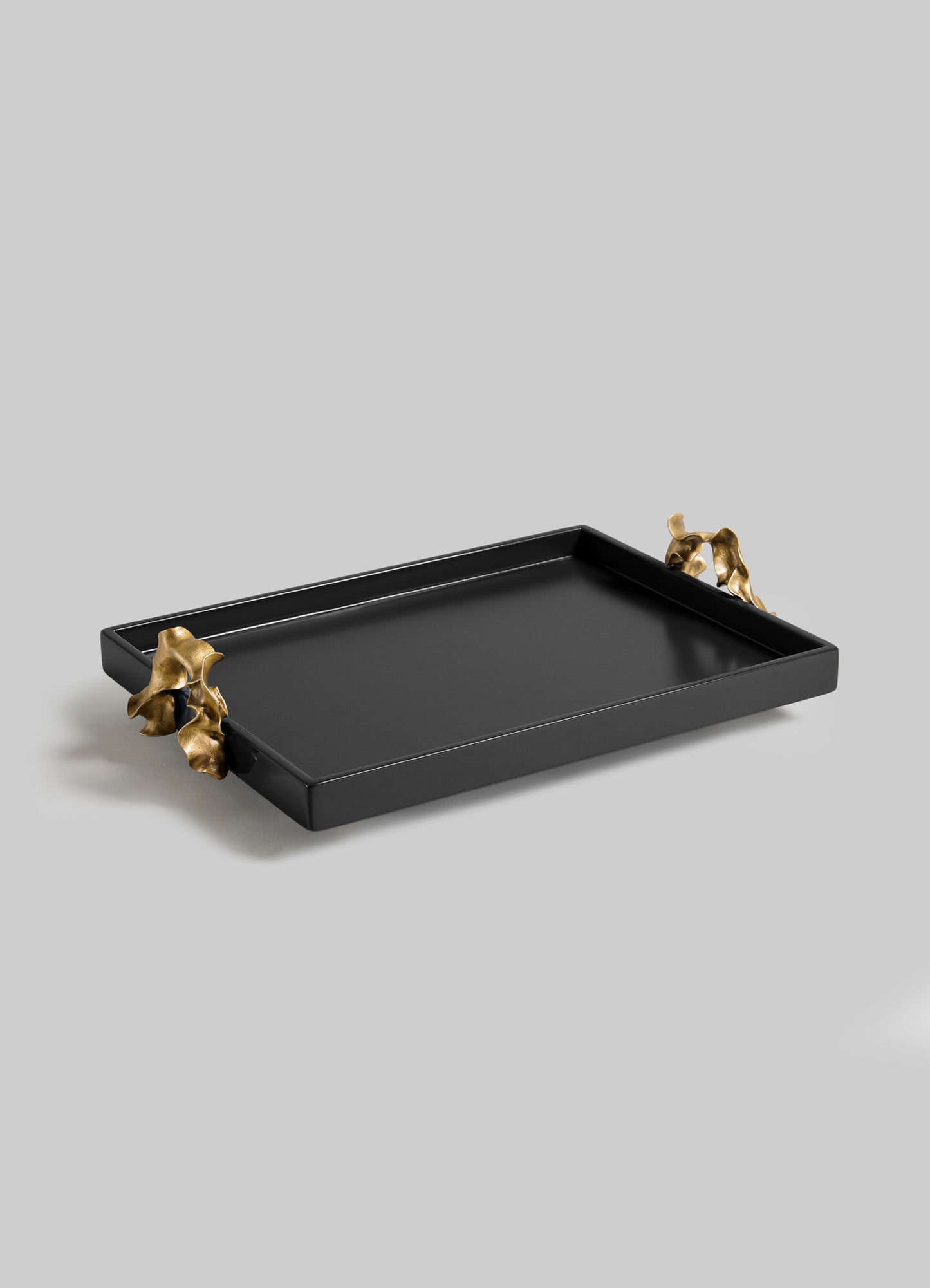 The VIYA Saffron Black Towel Tray features a rectangular black design with two gold handles shaped like abstract, contemporary bronzed forms, displayed against a light gray background.