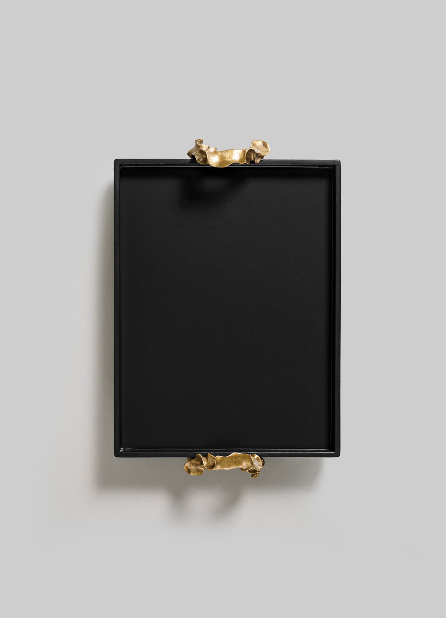 The Saffron Black Towel Tray by VIYA is a square black tray featuring two sculptural gold handles on opposite sides, styled like contemporary bronzed objects and displayed on a plain light gray background.