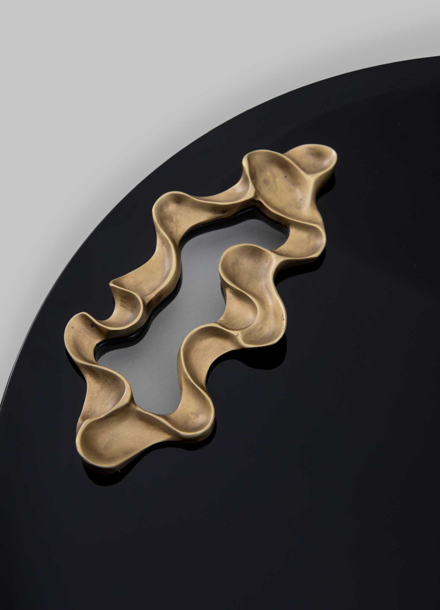 The VIYA Saffron Black Tray Large, featuring a glossy black finish, displays a wavy, abstract contemporary bronzed object against a light gray background.