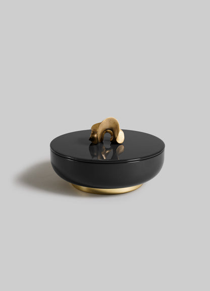 The VIYA Saffron Black Trinket Box Large is a round black container with a lid, featuring an abstract gold handle and matching gold base, elegantly set against a plain light gray background.