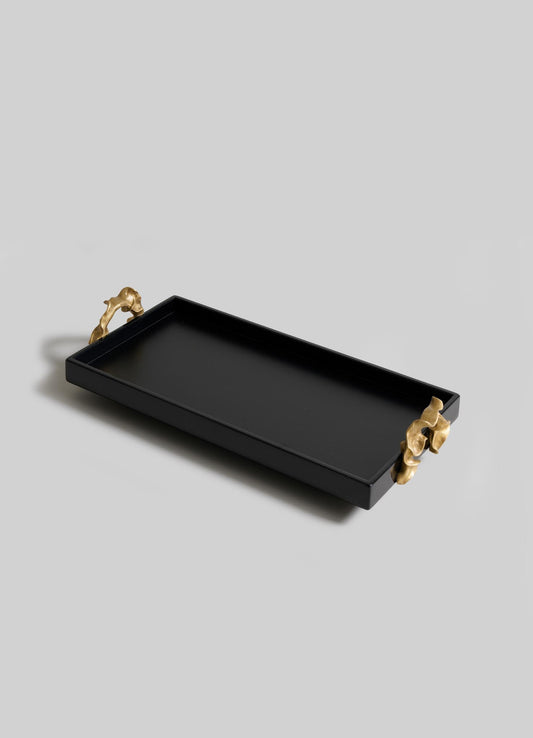 The VIYA Saffron Black Vanity Tray features a rectangular black design with raised edges and two decorative gold handles, inspired by trays once used for saffron in ancient Indian medicine, shown on a light gray surface.