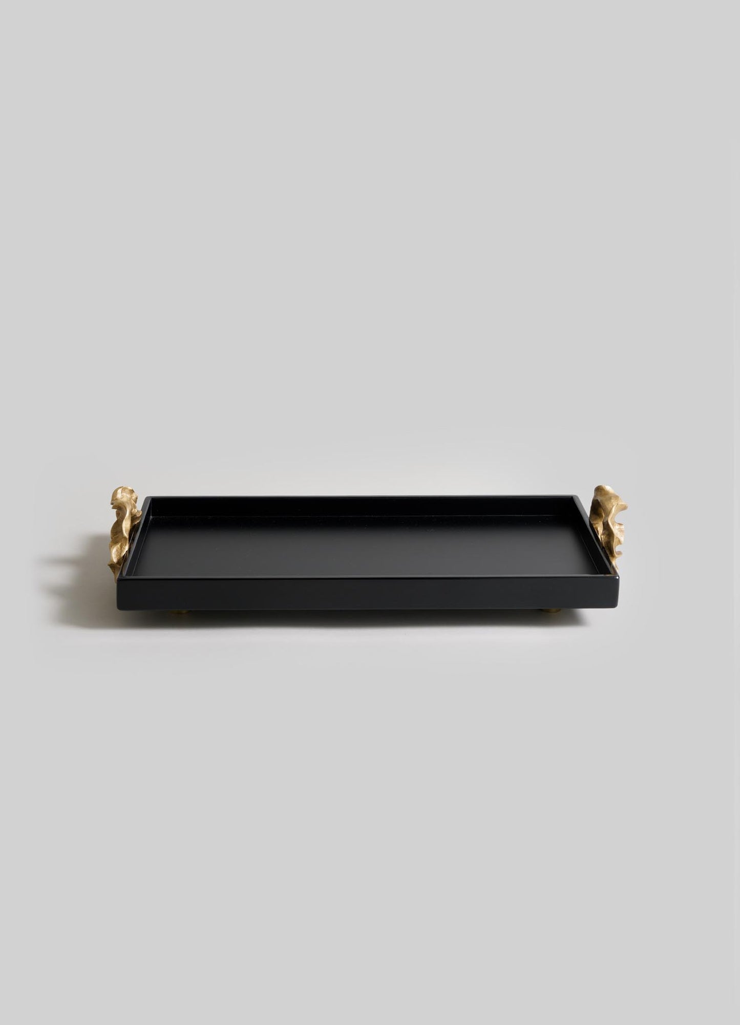 The VIYA Saffron Black Vanity Tray features a rectangular black design with raised edges and gold animal-shaped handles, inspired by ancient Indian medicine, and is beautifully displayed on a light gray background.